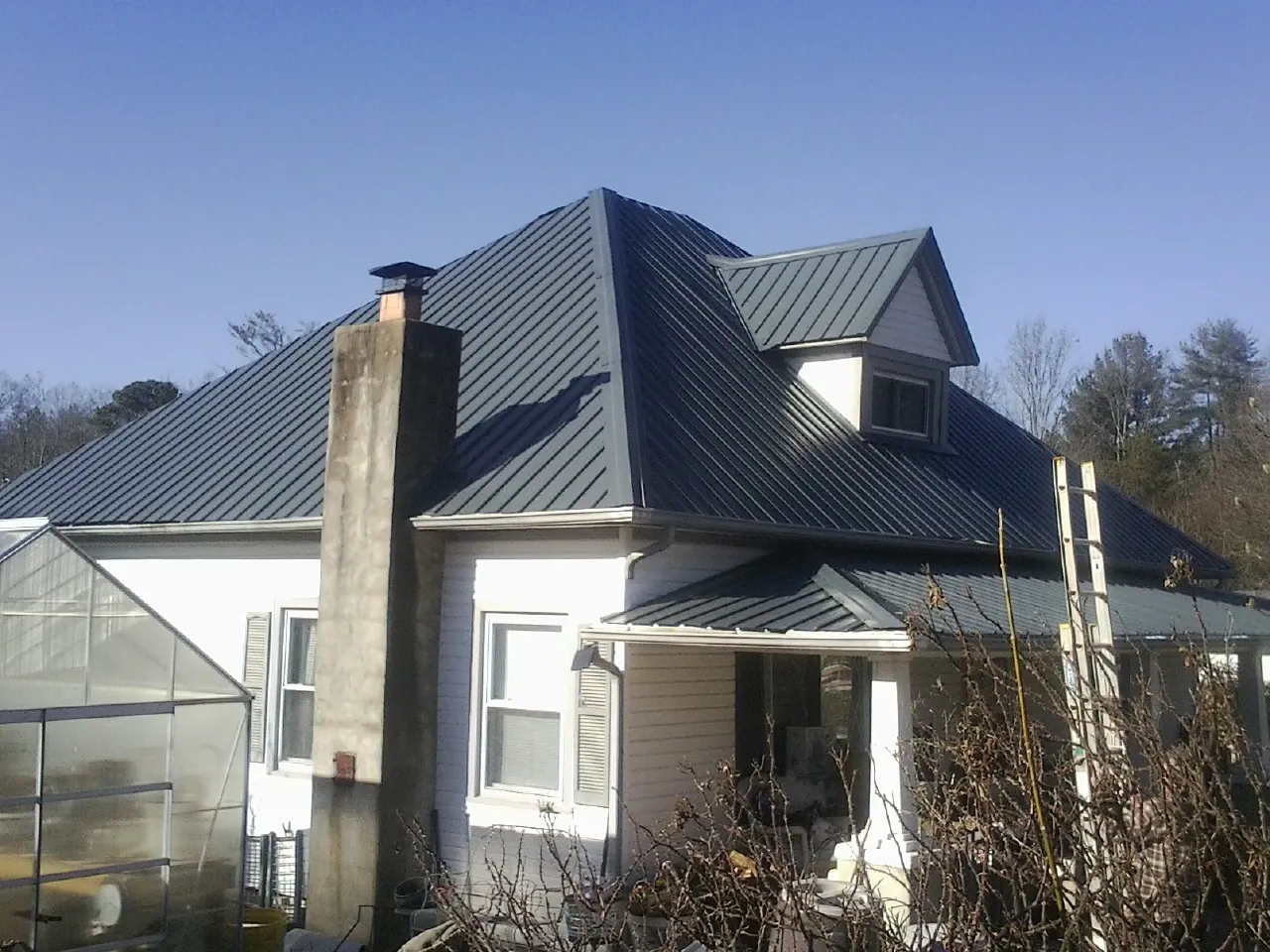 Dark blue standing seam metal roof on a white farmhouse with dormer — Slate & Tile Roof Repair by Roofing Brothers in Keezletown