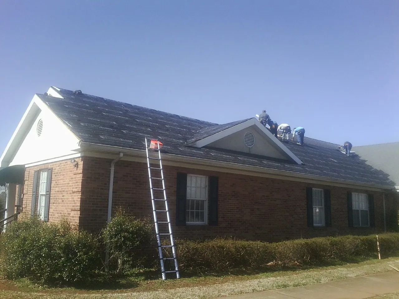 Crew tearing shingles off a brick ranch roof with a ladder set — Metal Roof Repair work by our crew in Keezletown