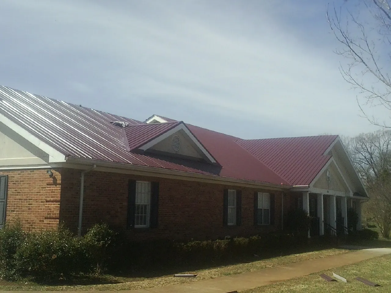 Red metal roof with gabled entries on a long brick building, from a Hail Damage Roof Repair job in Keezletown