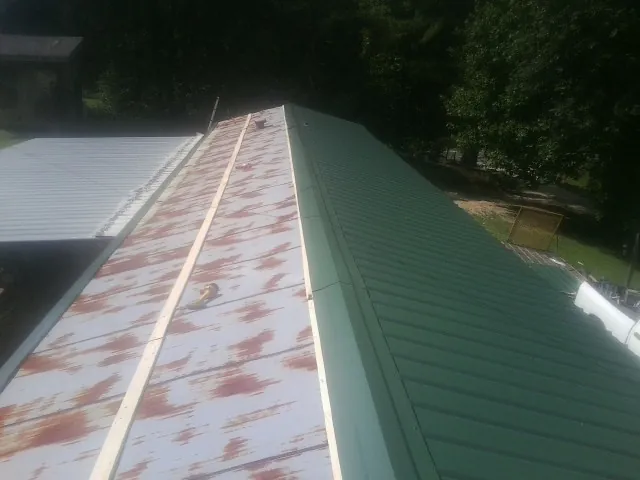 Old rusted panels beside newly installed green metal roofing — Wind Damage Roof Repair by Roofing Brothers in Keezletown