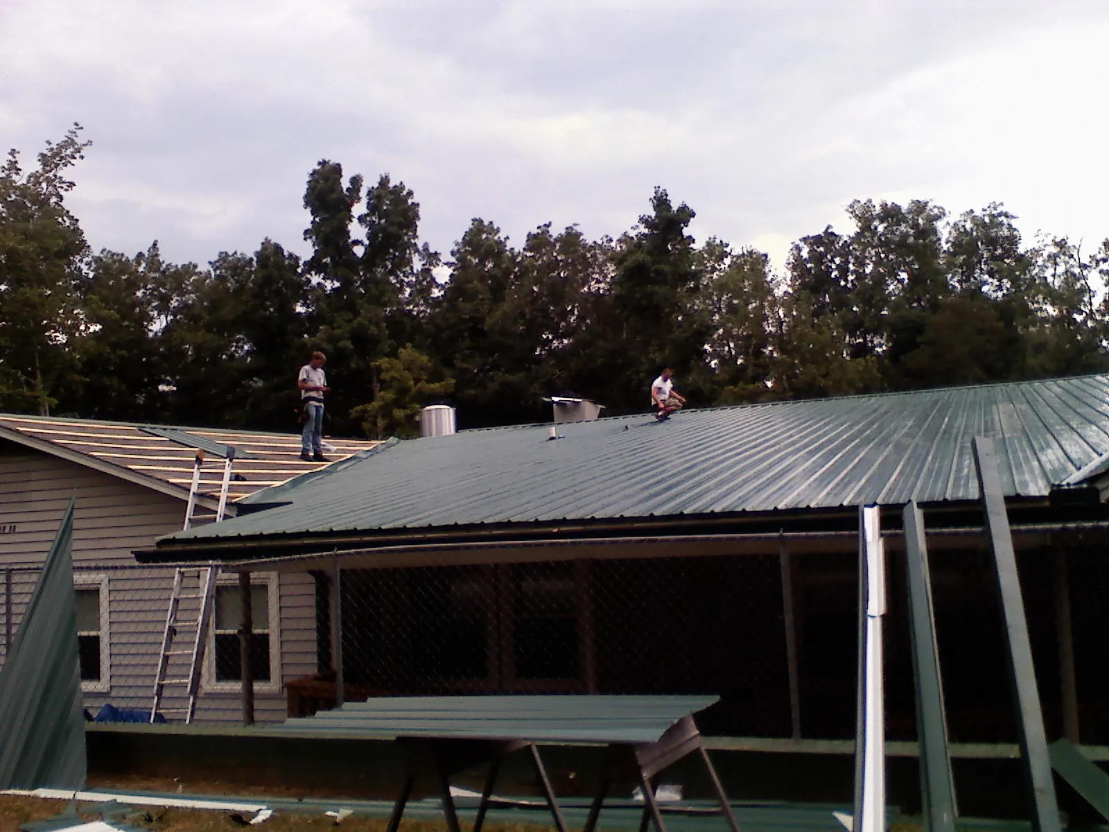 Two roofers installing green metal panels above a covered porch in Keezletown