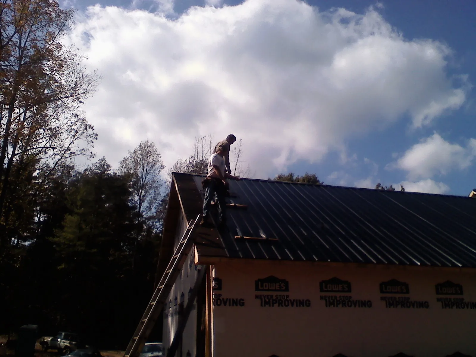 Roofer fastening dark metal panels high against a cloudy sky, from a Roof Inspection job in Keezletown