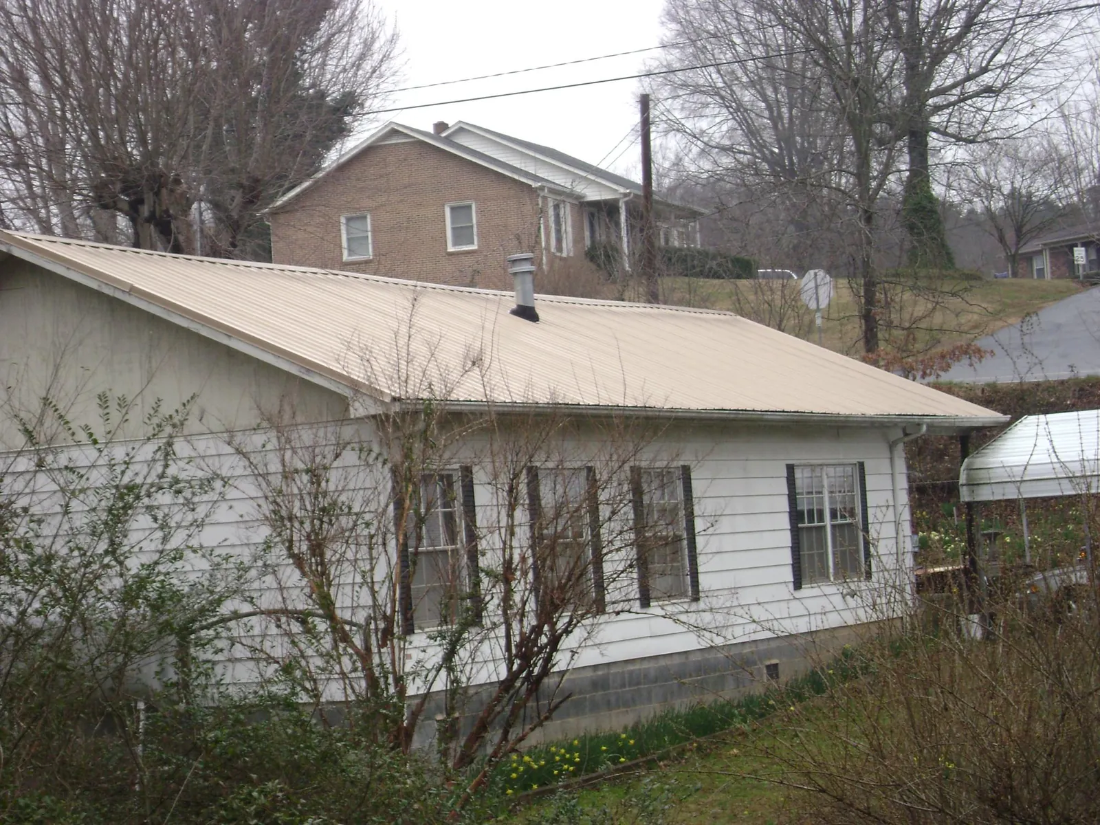 Tan metal roof on a white sided house set into a hillside — Commercial Roofing by Roofing Brothers in Keezletown